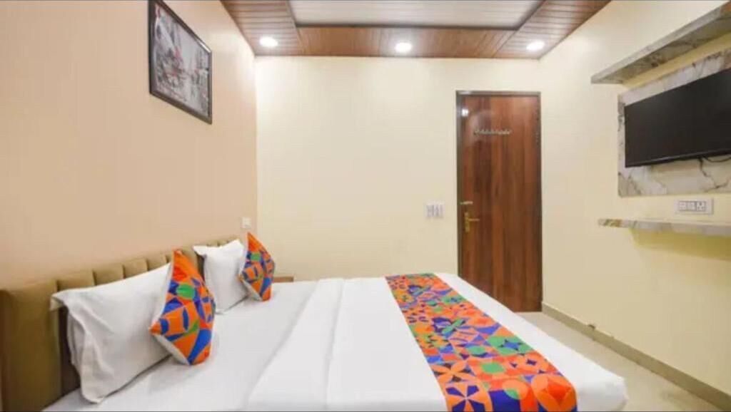 Una habitación de hotel con cama, almohadas, una puerta y un televisor fijado a la pared.