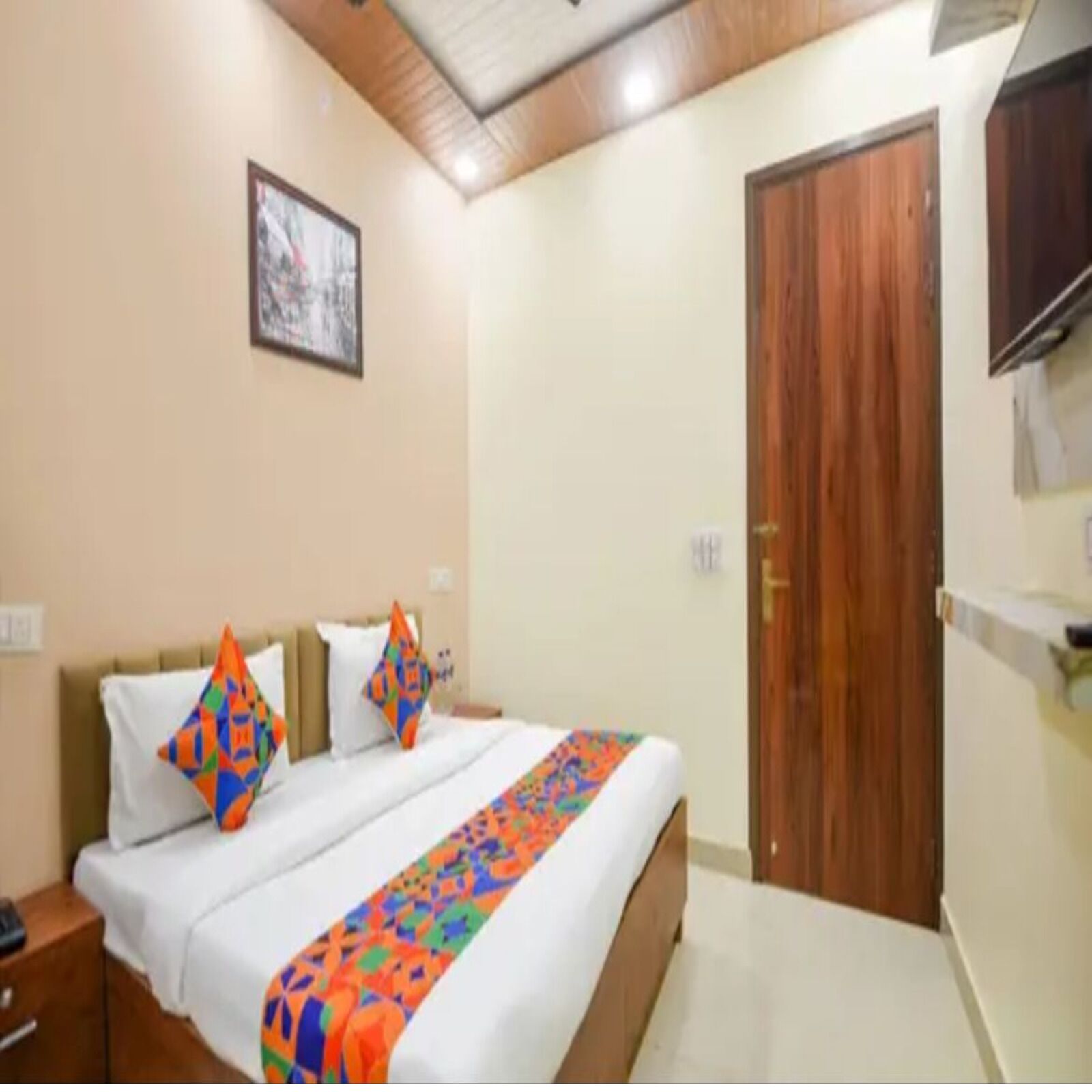 A hotel room with a bed, a wooden door, and a television on the wall.