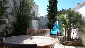 Una mesa de madera con sillas, un muro de piedra y un árbol alto en un patio.