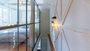 Ein modernes Schlafzimmer mit Glastrennwand, Holzboden und einem Bett mit gestreifter Bettwäsche.