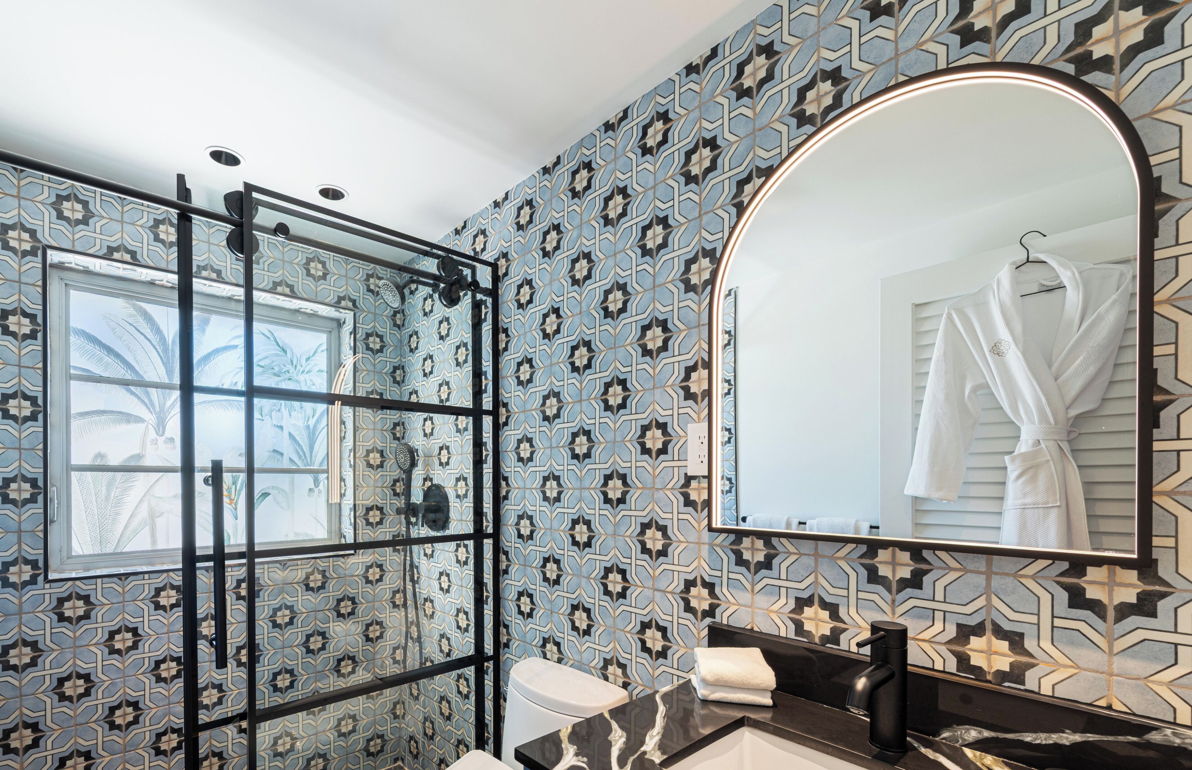A bathroom with patterned tiles, a glass shower enclosure, a large mirror, and a towel on the counter.