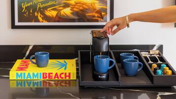 Ein Tablett mit einer Kaffeemaschine, blauen Tassen und einem Buch mit dem Titel 'MIAMI BEACH' auf einer spiegelnden Oberfläche.