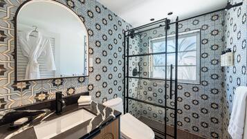 Ein Badezimmer mit Marmorwaschbecken, Toilette, einer Duschkabine aus Glas und Wandverkleidungen mit Muster.