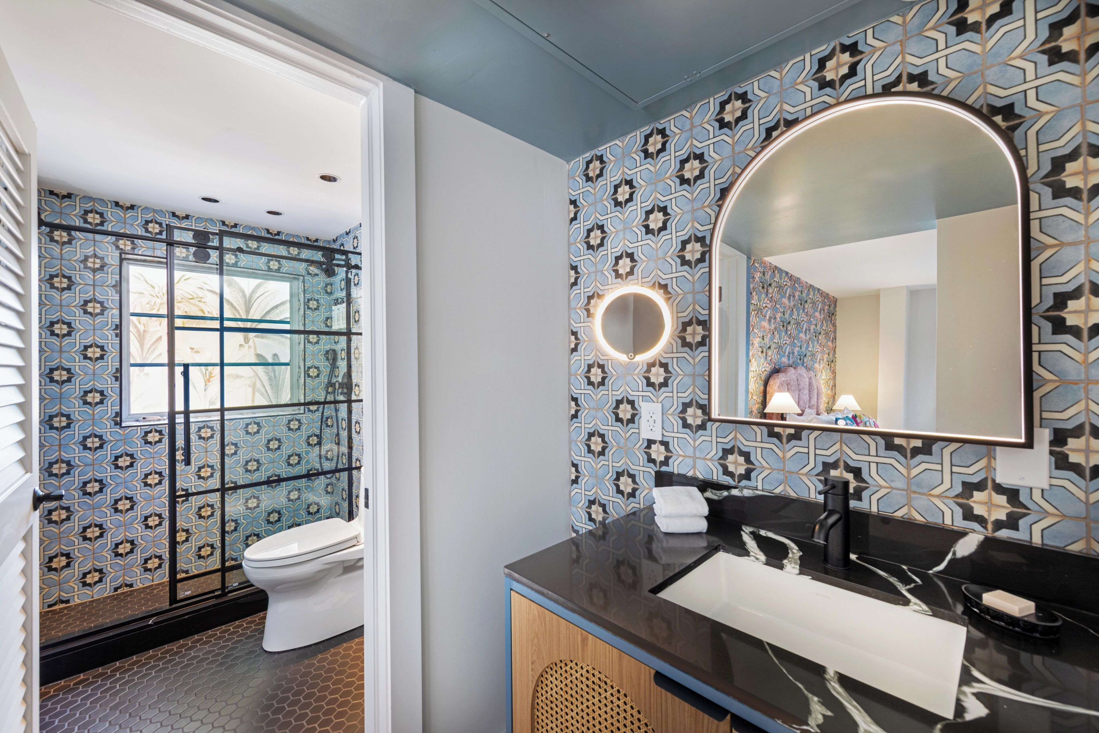 Une salle de bain avec des carreaux décorés, des toilettes, un lavabo avec un miroir et un luminaire rond.