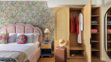 Une chambre à coucher avec un lit, une table de chevet, une valise, une armoire et un mur orné d’un motif tropical.