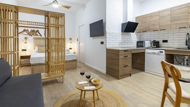 A compact living space with a kitchenette, a dining area with a round table, and a bed with a wooden headboard. - Travel Habitat Nou Mestalla 4 (Valencia)
