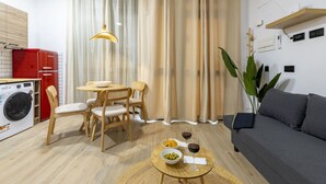 A compact living space with a dining area, a sofa, a washing machine, and a dining table with a bowl of olives and a glass of wine. - Travel Habitat Nou Mestalla 4 (Valencia)