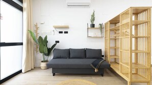 A modern living room with a dark grey sofa, a wooden bookshelf, a large potted plant, and a round woven rug. - Travel Habitat Nou Mestalla 4 (Valencia)