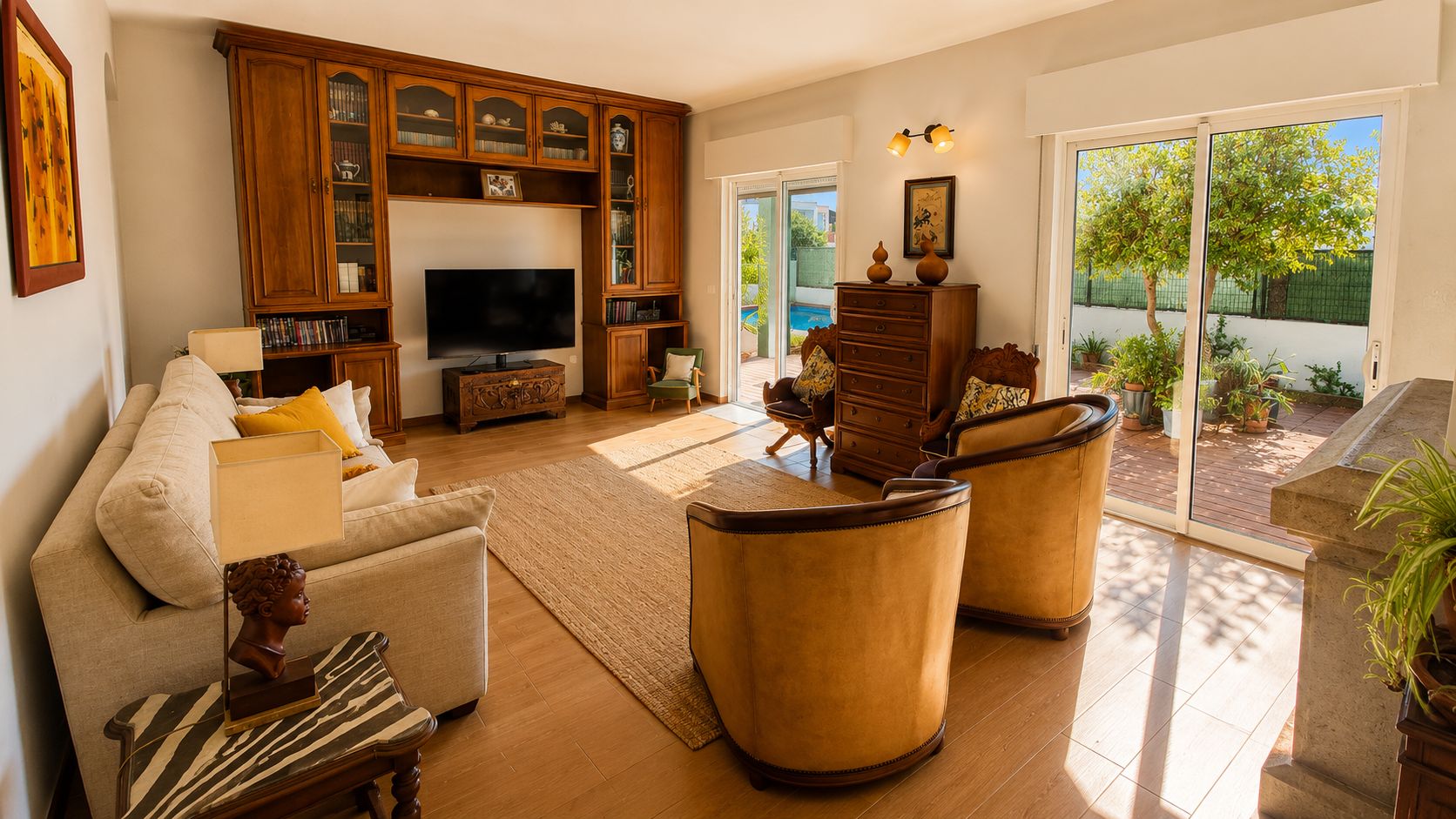 A living room with a sofa, armchairs, a TV, wooden cabinets, and a view of the outdoors.
