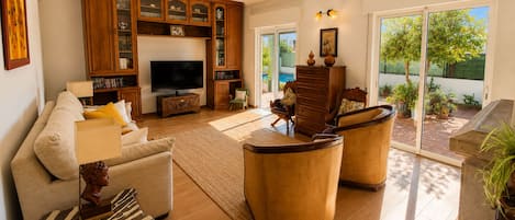 A living room with a sofa, armchairs, a TV, wooden cabinets, and a view of the outdoors.