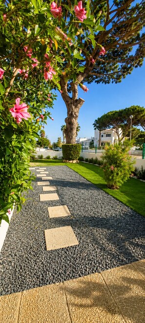 A pathway with stepping stones leading to a tree with pink flowers, surrounded by greenery and buildings in the background. - Exclusive Villa with Pool - Boat Tour Included in the Reservation* (Faro)