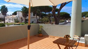 Un patio con un paraguas color arena, una mesa de madera y un banco.