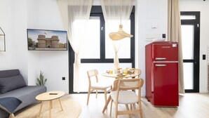 A modern living room with a sofa, round table, chairs, a red refrigerator, and a large window with sheer curtains. - Travel Habitat Nou Mestalla 3 (Valencia)