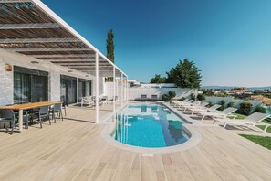 Et moderne poolområde udendørs med træterrasse, liggestole og spisebord.