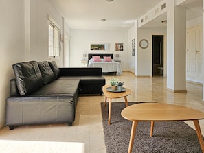 Un salon moderne avec un canapé en cuir, une table basse ronde en bois et un lit recouvert d’une couvre-lit à rayures.