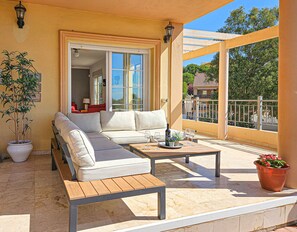 Un balcon ensoleillé avec un canapé blanc, une table en bois et une plante en pot.