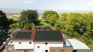 Een modern gebouw met een rood dak, zonnepanelen en uitzicht op een meer.