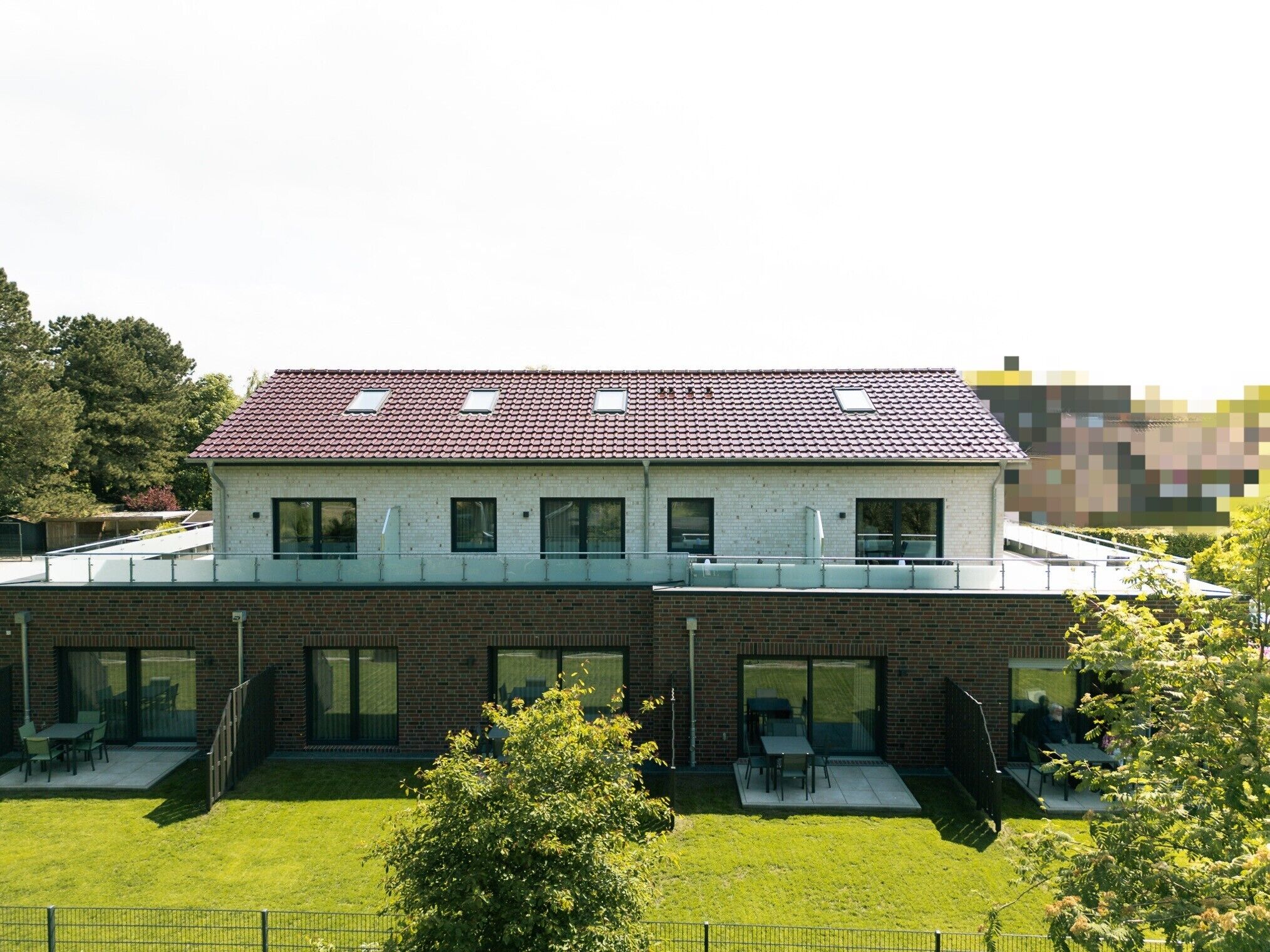 A modern building with a red-tiled roof, large windows, and a flat roof terrace.