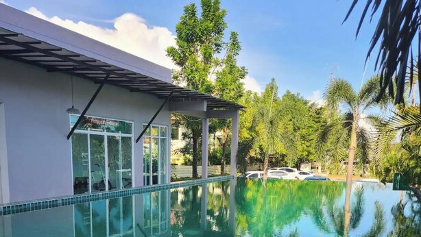 A clear swimming pool with a tiled edge, a covered seating area, and surrounding greenery. - Charming Condo in Wichit Comfort Meets Convenience (Wichit)