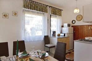 A dining area with a table set for four, a kitchen with basic appliances, and a clock on the wall. - Spacious Apartment With Parking (Umag)