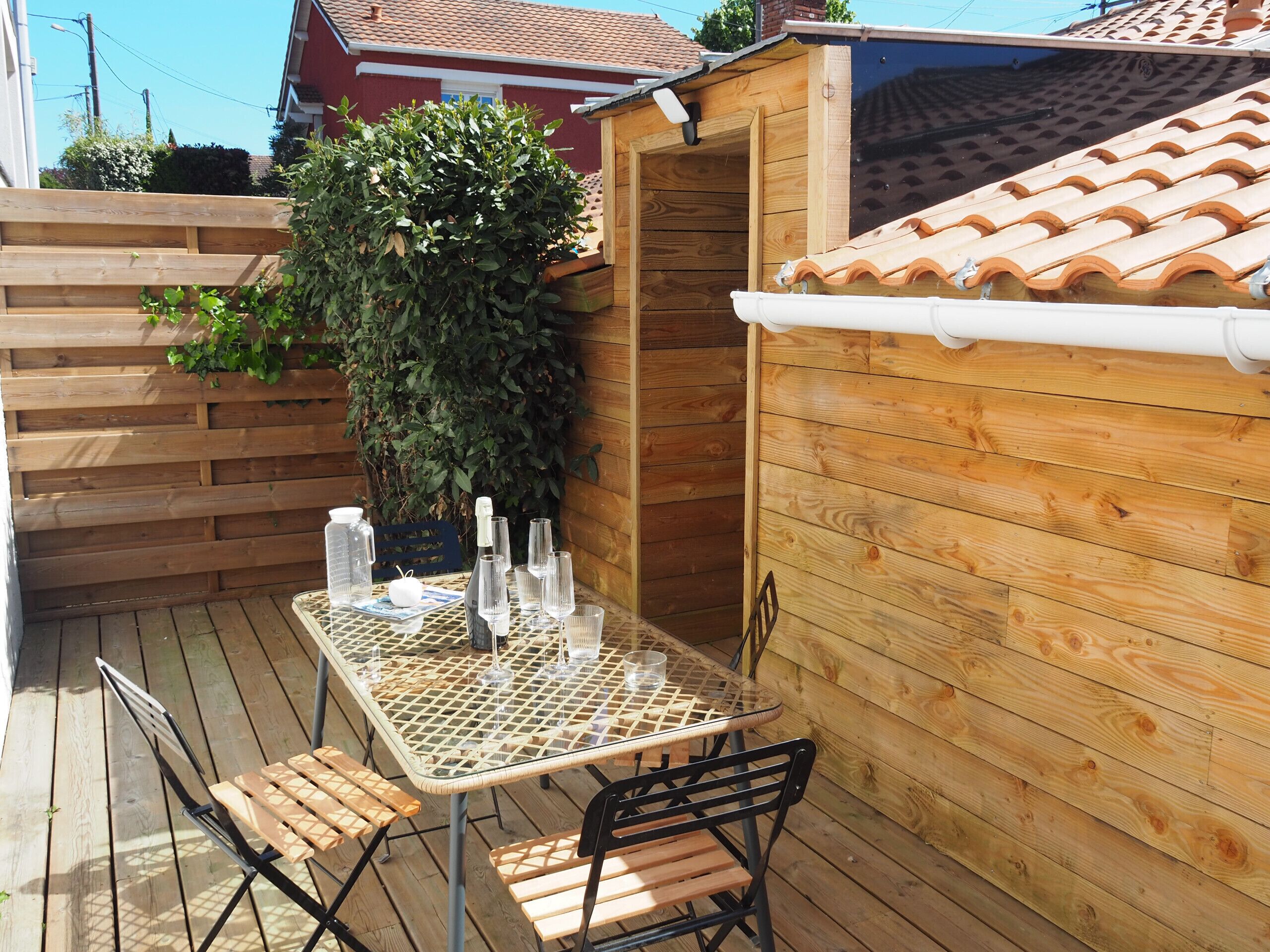 A wooden deck with a table and chairs, a potted plant, and a small wooden structure.