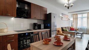 A modern kitchen with wooden cabinets, a built-in oven, and a dining area with a table set for four. - RentPlanet - Apartament Pomorska (Wrocław)