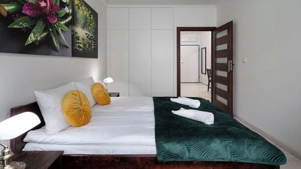 A neatly made bed with white linens, two yellow pillows, a green throw blanket, and two neatly folded towels. - RentPlanet - Apartament Pomorska (Wrocław)