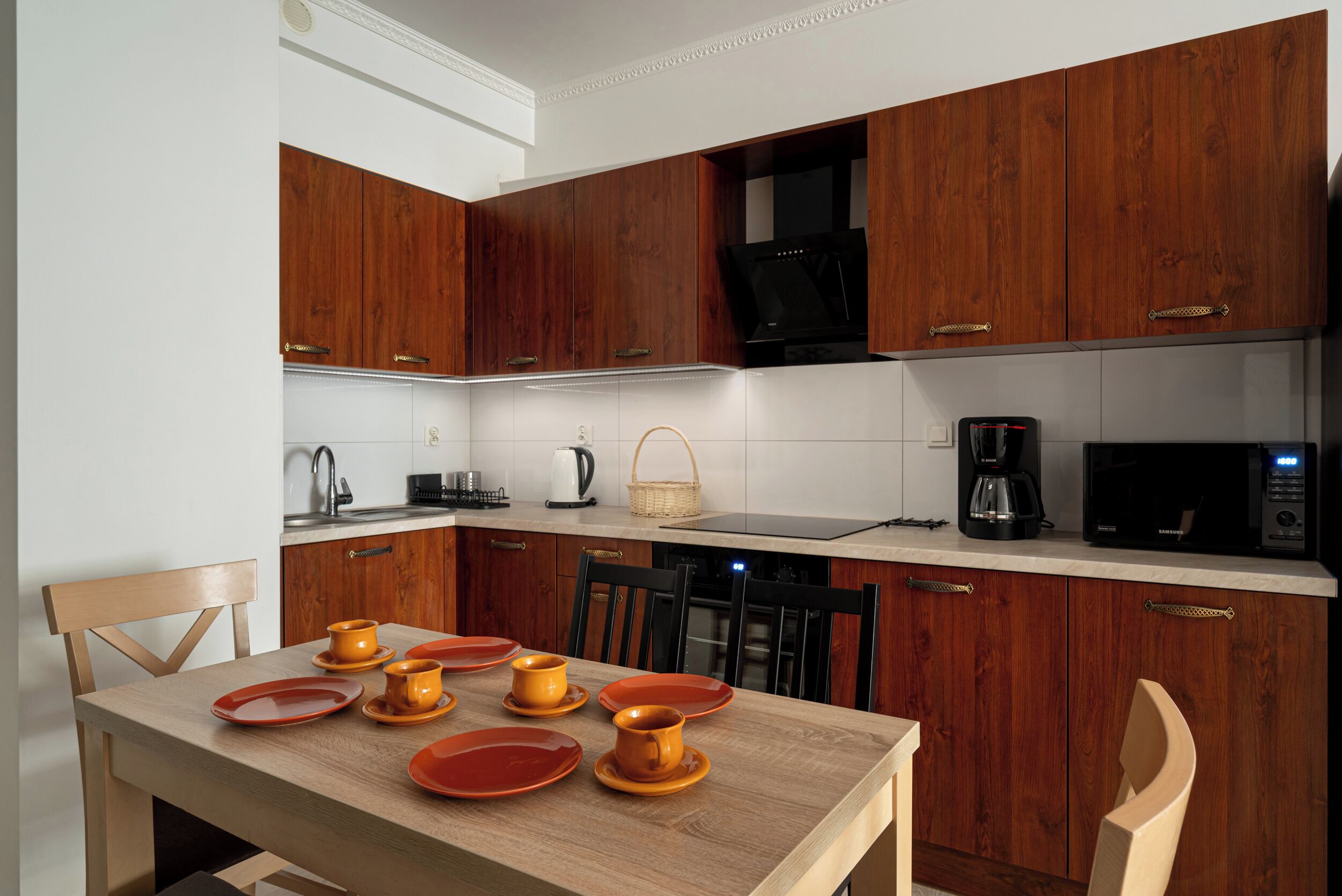 Une cuisine moderne avec des meubles en bois, une table à manger dressée avec des assiettes et des tasses orange, et une machine à café.
