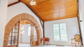 A spacious room with a high wooden ceiling, large arched doorway, and a chandelier. - Aile château de Saint-Sarnin - 14 pers, 5 chambres. piscine. parc & nature (Grisolles)