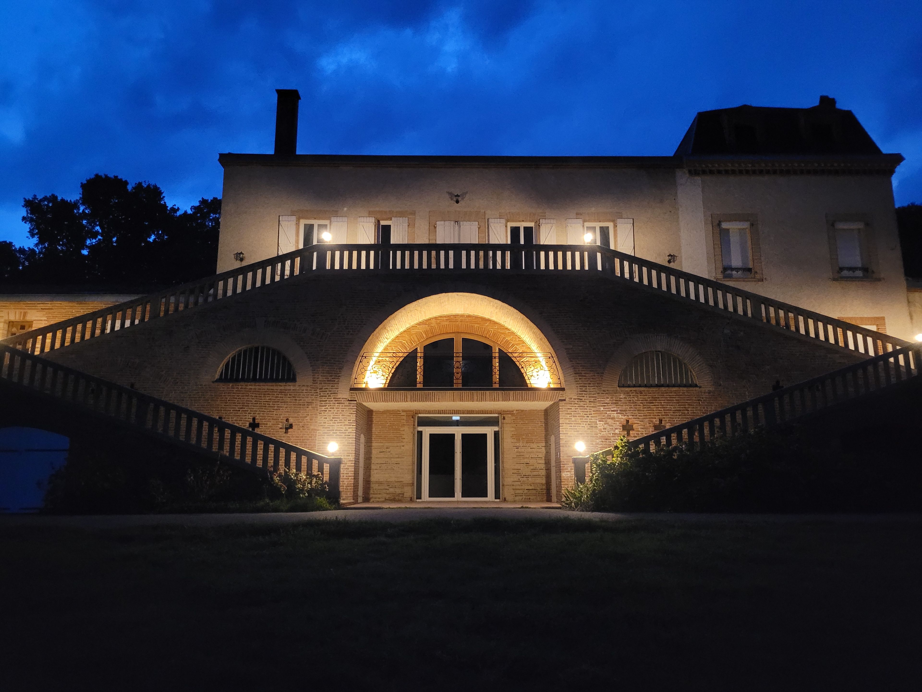 A building with a prominent arched bridge entrance, a balcony with railing, and a chimney.