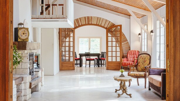 A spacious interior with a high ceiling, wooden beams, a fireplace, a dining area, and a staircase leading to an upper level. - Aile château de Saint-Sarnin - 14 pers, 5 chambres. piscine. parc & nature (Grisolles)