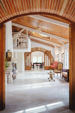A spacious interior with a high ceiling, wooden beams, a fireplace, a dining area, and a staircase leading to an upper level. - Aile château de Saint-Sarnin - 14 pers, 5 chambres. piscine. parc & nature (Grisolles)