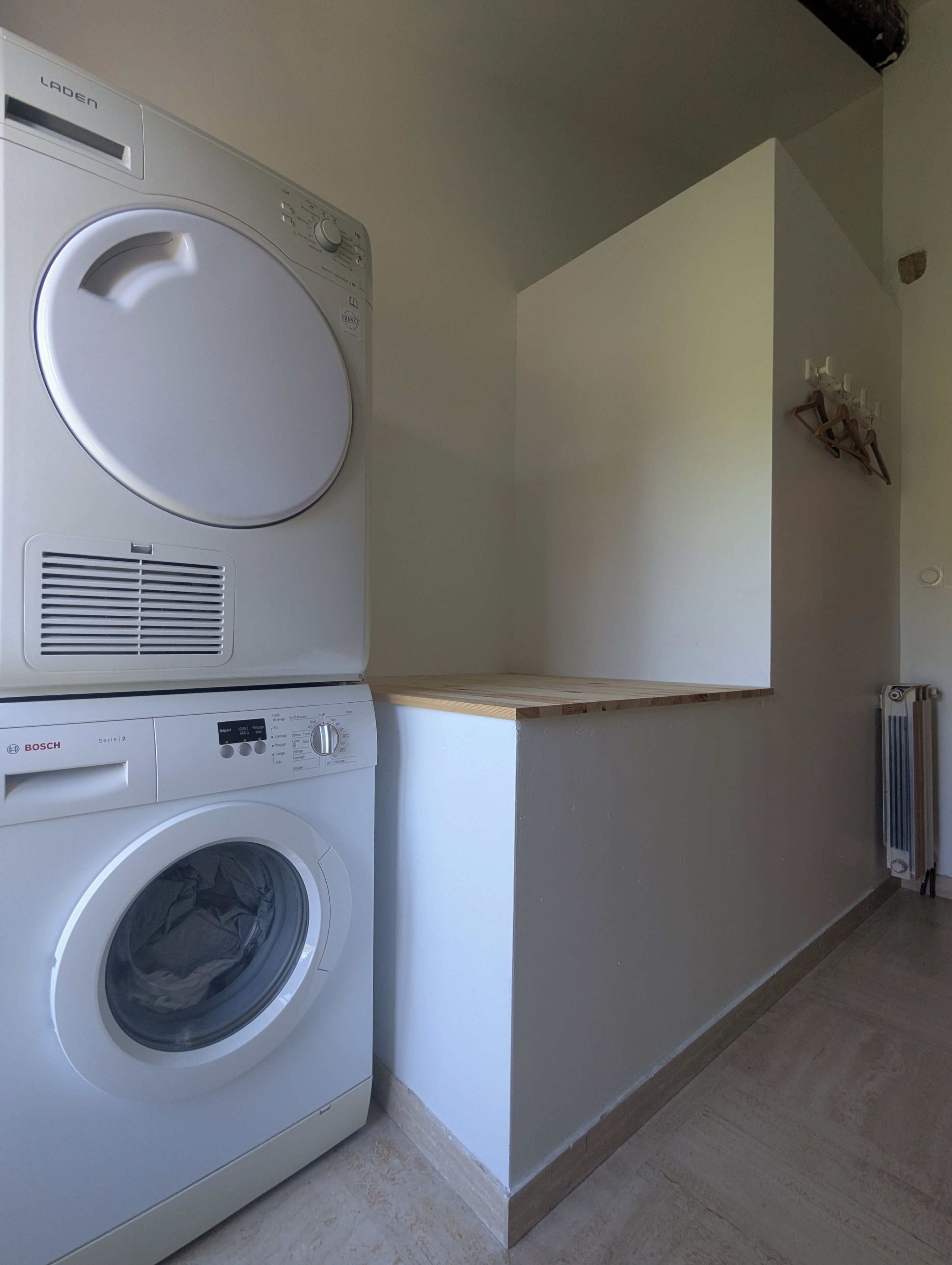A laundry area with a Bosch washing machine and a dryer, a wooden countertop, and a radiator.