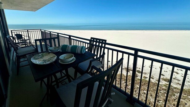 Een balkon met een tafel, stoelen en uitzicht op het strand.