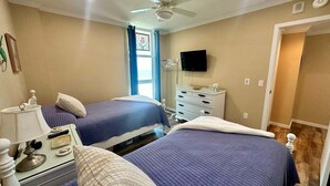 Een kamer met twee bedden, een plafondventilator, een televisie en een dressoir.
