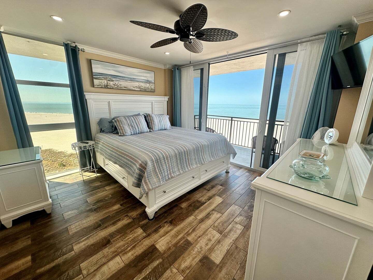 Un dormitorio con cama, ventilador de techo, televisor y vista a la playa.