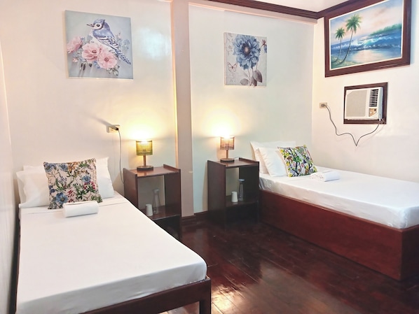 Una habitación de hotel con dos camas individuales, una mesita de noche con lámpara, una pequeña mesa y aire acondicionado instalado en la pared.