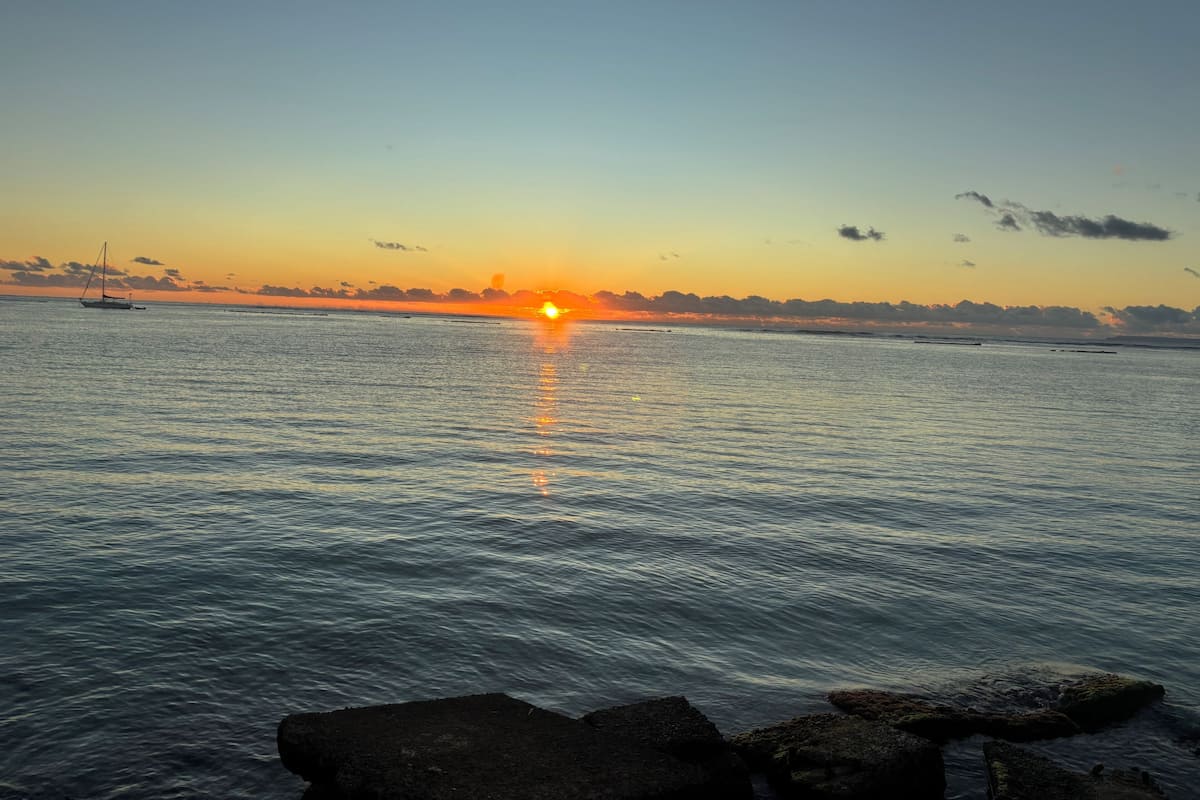 Atardecer sobre un mar tranquilo con un velero y costa rocosa.