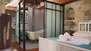 A bedroom with a bed, a bathroom with a bathtub, and a stone wall. - Authentic Zakynthos Town Villa * 3 open-plan bedrooms * Sleeps <7 * Local Stay (Zakinthos)