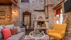 A cozy room with a stone wall, a fireplace, a sofa, a yellow armchair, and a glass coffee table. - Authentic Zakynthos Town Villa * 3 open-plan bedrooms * Sleeps <7 * Local Stay (Zakinthos)