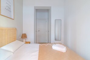 Een hotelkamer met een bed, een nachtkastje met een lamp, een deur en een spiegel.