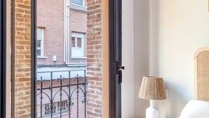 Ein Hotelzimmer mit Blick auf ein Backsteingebäude, ein Balkon mit schmiedeeisernem Geländer und ein Nachttisch mit Lampe.