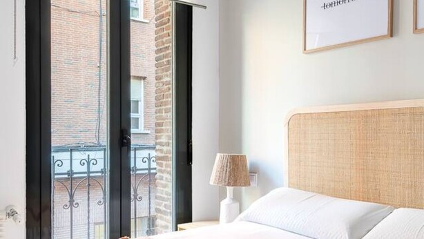 Ein Schlafzimmer mit Bett, Nachttisch, Lampe und Blick auf ein Backsteingebäude durch eine Glastür.
