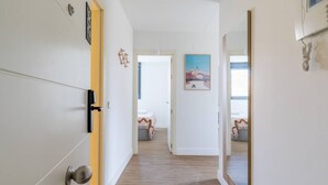 Ein Korridor mit Holzboden, weißen Wänden und einer Tür zu einem Schlafzimmer mit Bett und Fenster.