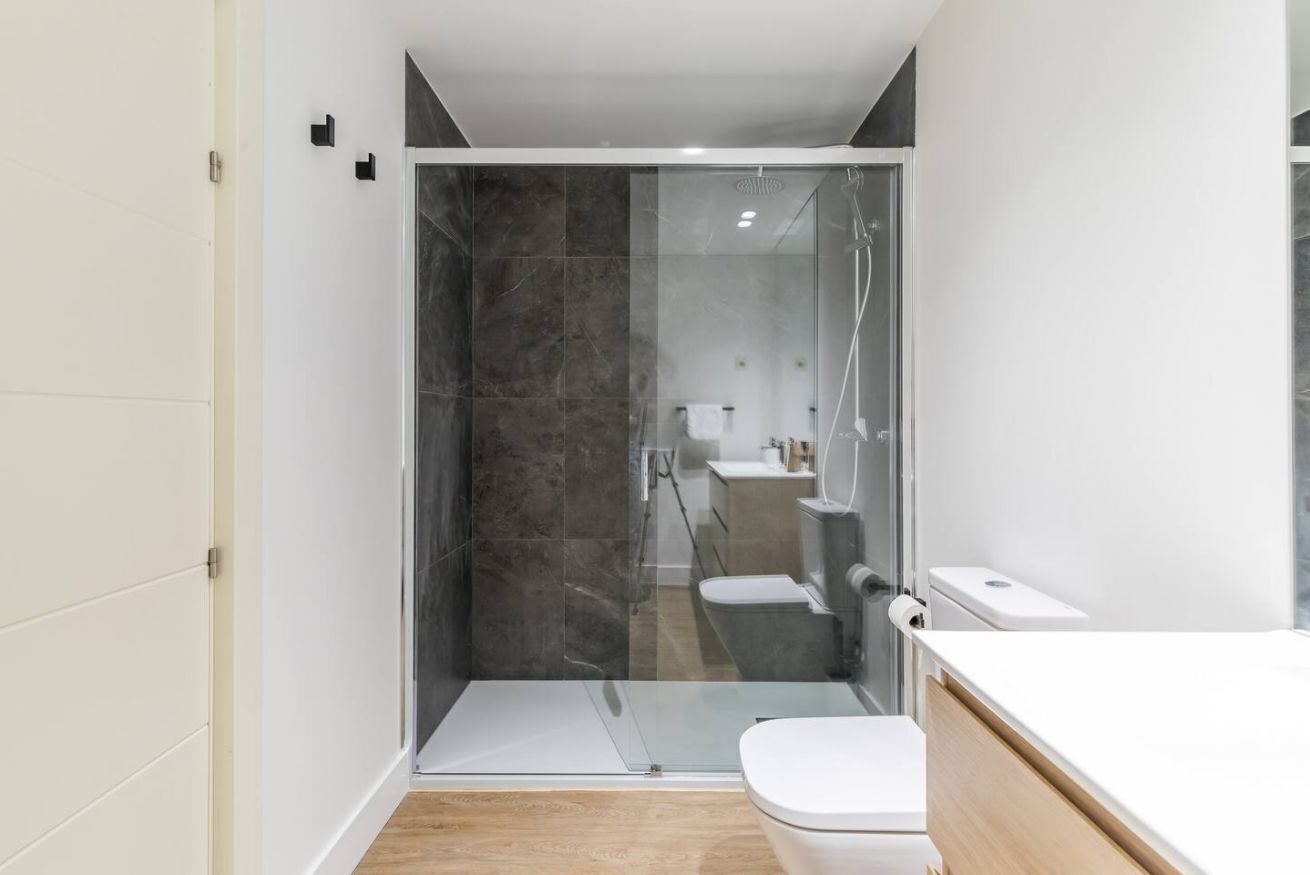 Une salle de bain moderne avec une douche à parois de verre, des toilettes blanches et un meuble-lavabo en bois avec un plan de travail blanc.