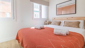Ein Hotelzimmer mit einem großen Bett, einem Fenster, einem Wandbild und einem kleinen Nachttisch.