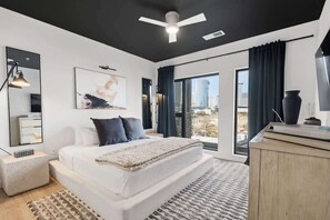 Ein modernes Schlafzimmer mit einem großen Bett, einem Deckenventilator, Blick auf die Stadt und einem großen Fenster mit Vorhängen.
