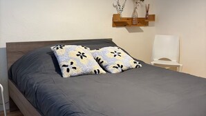 A neatly made bed with a dark grey bedspread and floral-patterned pillows, a wooden headboard, and a wall-mounted shelf with decorative items. - Le Relais de David - Limoges (Limoges)
