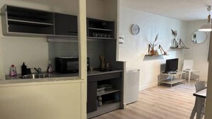 A compact kitchen with built-in appliances, a dining area with a table and chairs, and a small seating area with a TV and decorative items. - Le Relais de David - Limoges (Limoges)