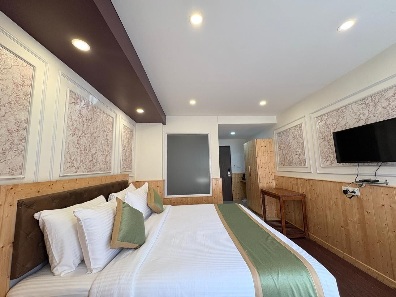 Une chambre d’hôtel avec un grand lit, une tête de lit en bois, une télévision et une armoire en bois.